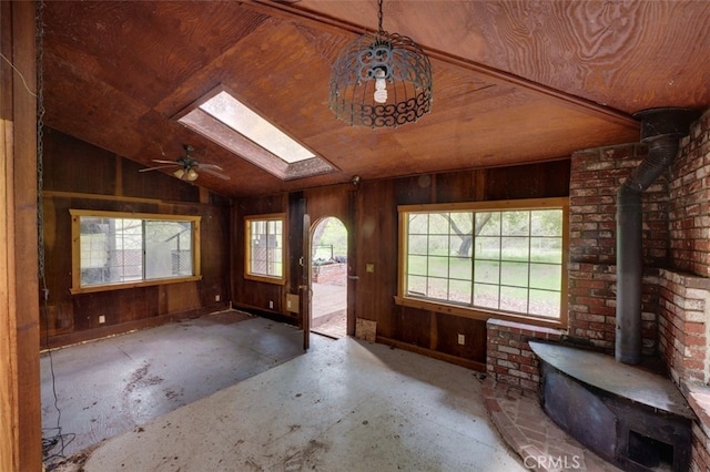 interior space with lofted ceiling with skylight, wood walls, and a wood stove