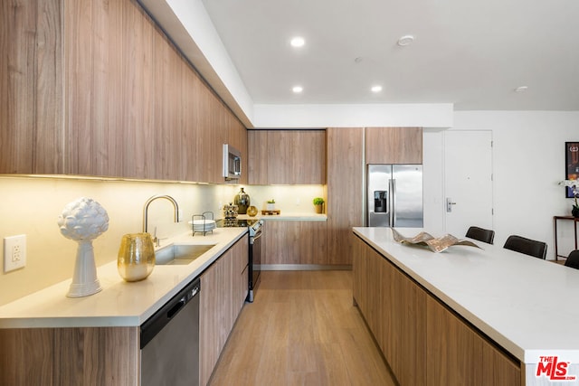 kitchen with a breakfast bar area, stainless steel appliances, a center island, light wood-type flooring, and sink