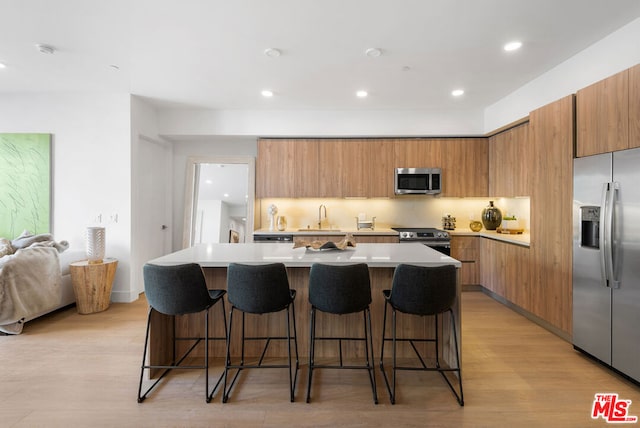 kitchen featuring light hardwood / wood-style flooring, appliances with stainless steel finishes, a center island, and a kitchen breakfast bar