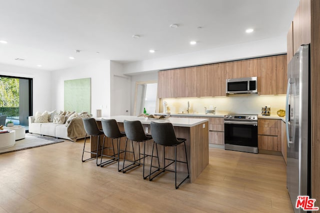 kitchen with a kitchen breakfast bar, appliances with stainless steel finishes, sink, light hardwood / wood-style flooring, and a kitchen island