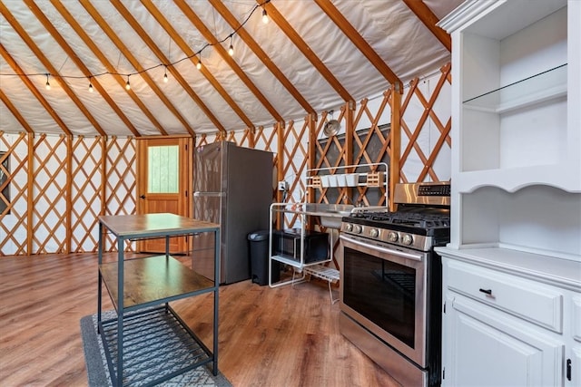 kitchen featuring vaulted ceiling, stainless steel range with gas stovetop, fridge, white cabinets, and hardwood / wood-style floors