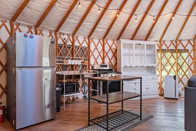 kitchen with vaulted ceiling with beams, wood-type flooring, appliances with stainless steel finishes, and white cabinets