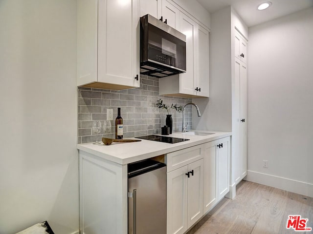 kitchen featuring sink, black electric stovetop, backsplash, light hardwood / wood-style floors, and white cabinetry