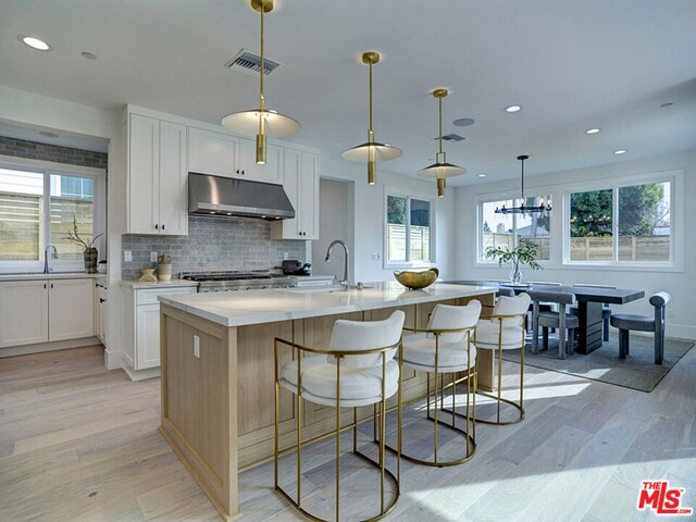 kitchen featuring white cabinets, a center island with sink, light hardwood / wood-style floors, and pendant lighting