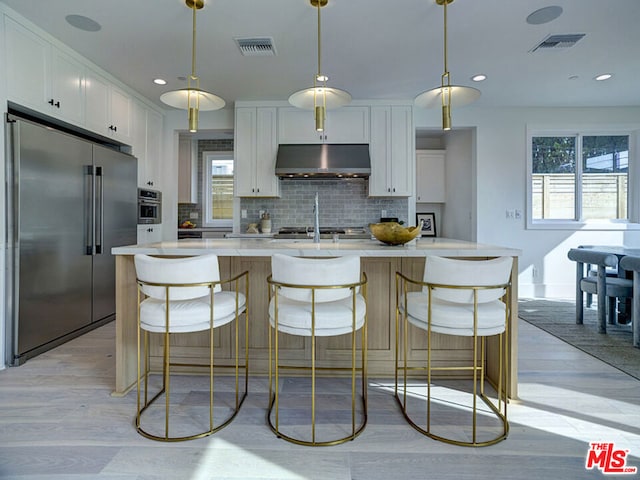 kitchen featuring white cabinets, appliances with stainless steel finishes, hanging light fixtures, and an island with sink