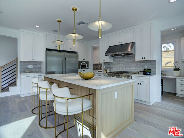 kitchen featuring a center island with sink, high end refrigerator, white cabinets, hanging light fixtures, and light wood-type flooring