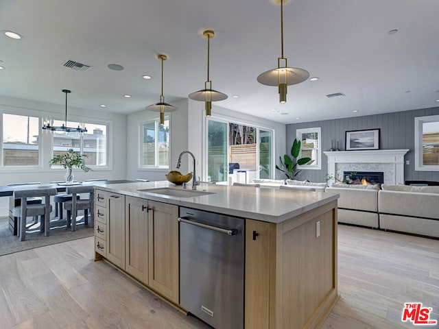 kitchen featuring stainless steel dishwasher, a center island with sink, hanging light fixtures, light wood-type flooring, and sink