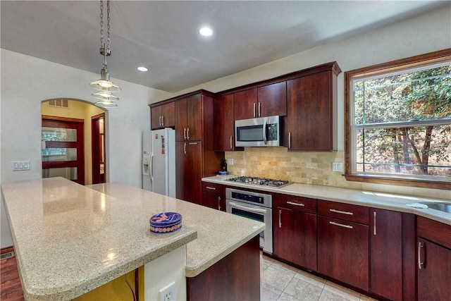 kitchen with arched walkways, light stone counters, stainless steel appliances, pendant lighting, and backsplash