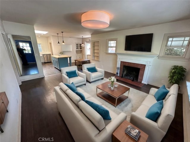 living room featuring a brick fireplace, plenty of natural light, and dark wood-type flooring