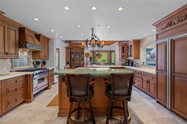 kitchen with custom exhaust hood, a breakfast bar area, premium stove, a kitchen island with sink, and backsplash