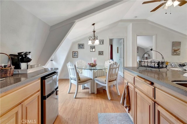 dining room featuring ceiling fan with notable chandelier, light hardwood / wood-style floors, and vaulted ceiling