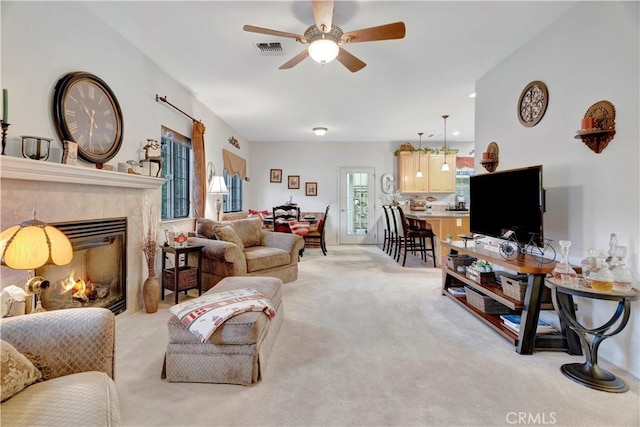 living room featuring light carpet, a tile fireplace, a healthy amount of sunlight, and ceiling fan