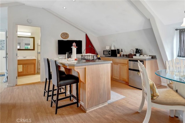 kitchen with light brown cabinetry, stainless steel appliances, light hardwood / wood-style flooring, and a center island with sink