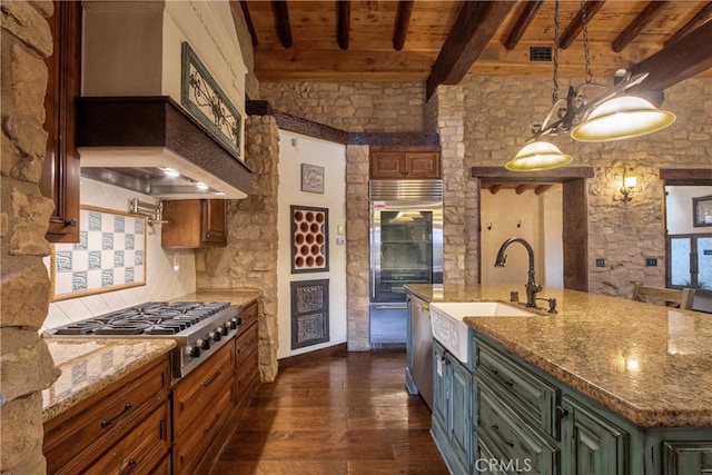 kitchen featuring appliances with stainless steel finishes, custom range hood, a kitchen island with sink, pendant lighting, and beam ceiling