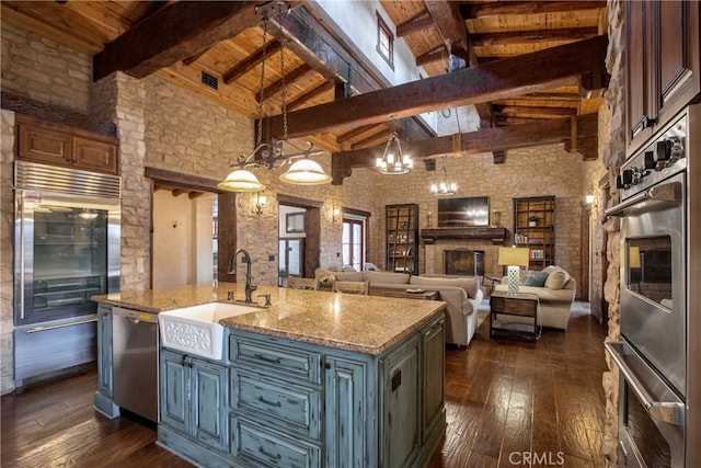 kitchen with dark wood-type flooring, a chandelier, beamed ceiling, a center island with sink, and hanging light fixtures