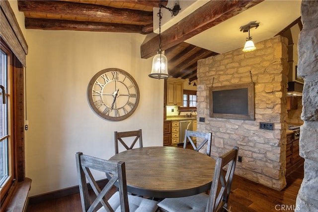 dining room with beam ceiling, a stone fireplace, and dark hardwood / wood-style flooring