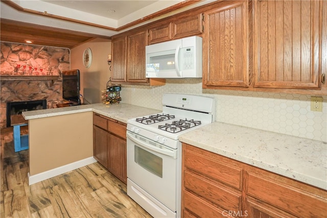 kitchen featuring kitchen peninsula, backsplash, light hardwood / wood-style flooring, a fireplace, and white appliances