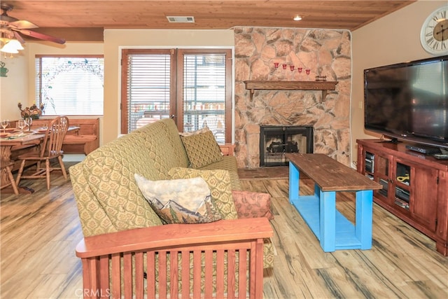 living room featuring plenty of natural light, a stone fireplace, wooden ceiling, and light wood-type flooring