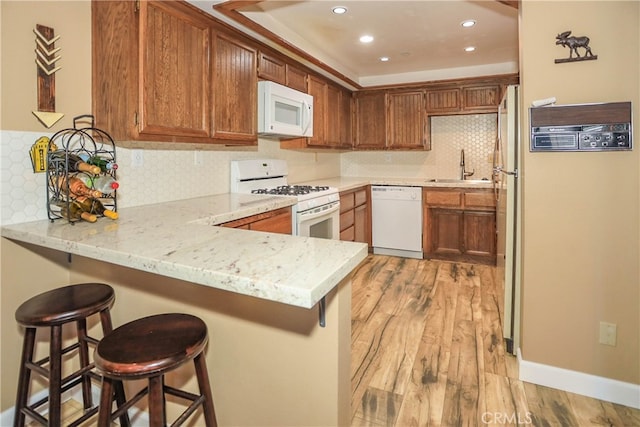 kitchen featuring white appliances, sink, a kitchen bar, kitchen peninsula, and light hardwood / wood-style flooring