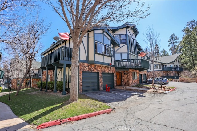 tudor-style house with a front yard, a balcony, and a garage