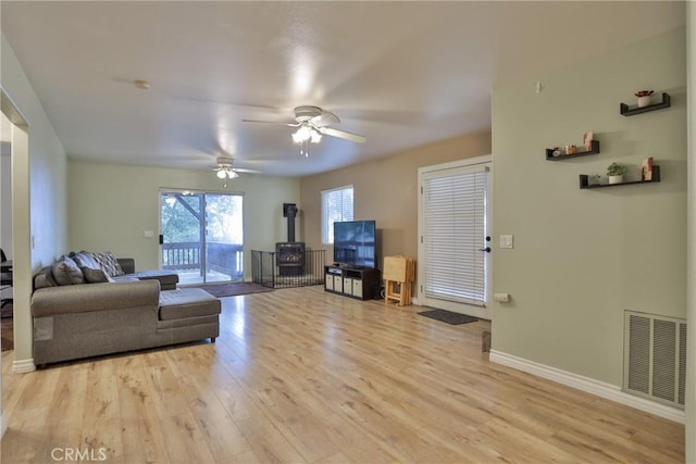 living room featuring a wood stove, ceiling fan, and light wood-type flooring