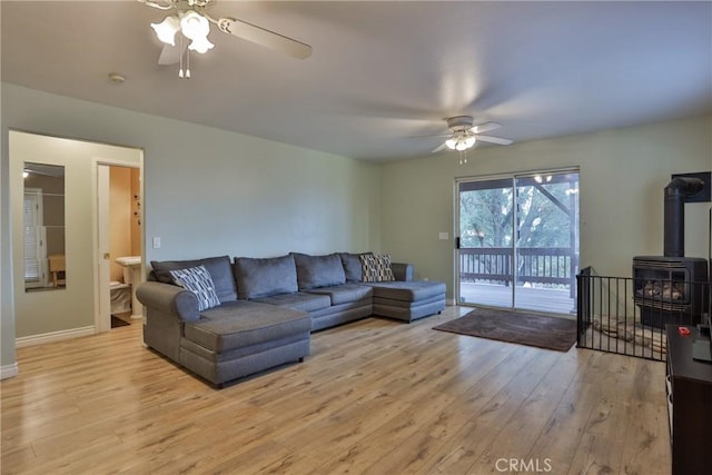 living room with light hardwood / wood-style floors, a wood stove, and ceiling fan