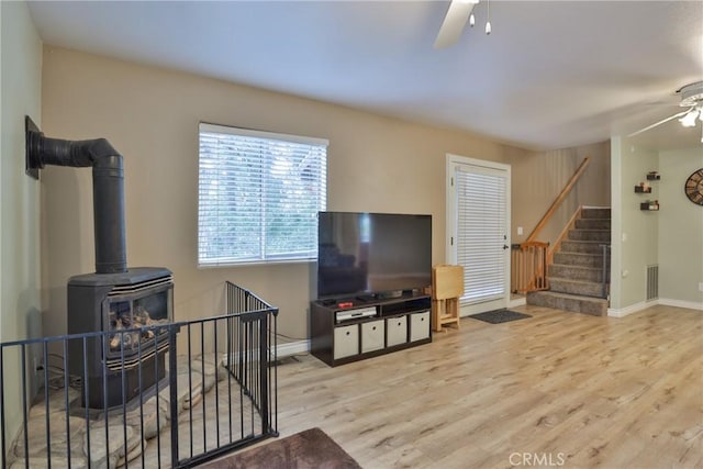 living room featuring ceiling fan, light hardwood / wood-style floors, and a wood stove