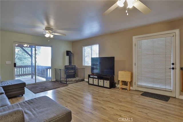 living room with a wood stove, ceiling fan, and light hardwood / wood-style flooring