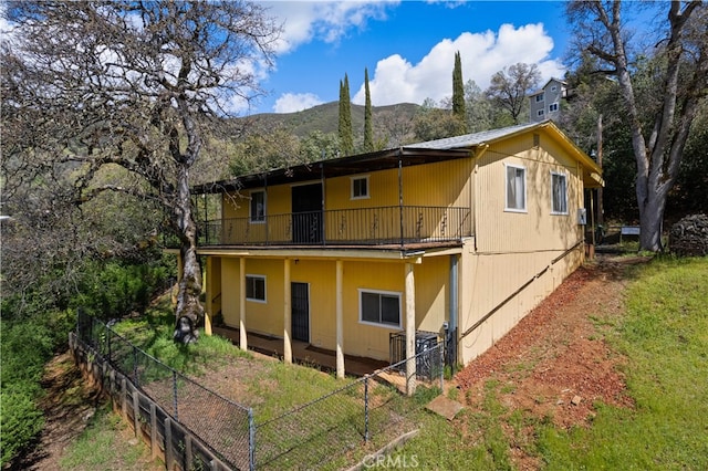 rear view of property with cooling unit, a mountain view, a balcony, and a lawn