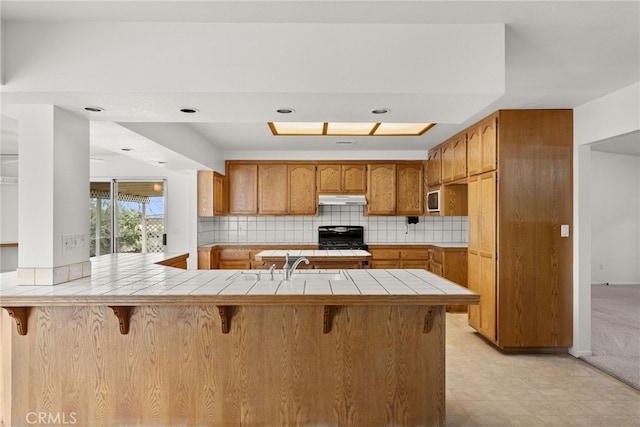 kitchen with black range, tile countertops, kitchen peninsula, and a breakfast bar