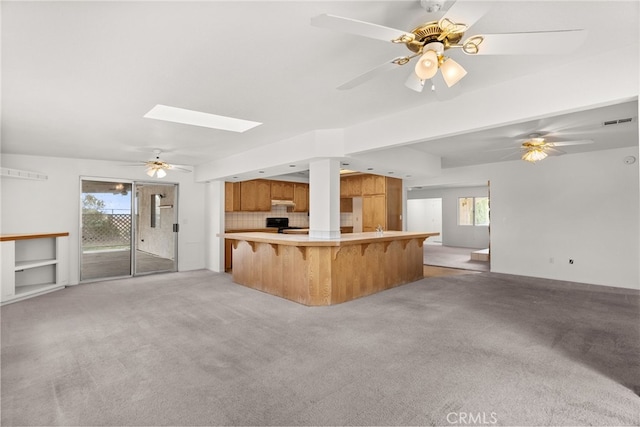 kitchen with light colored carpet, kitchen peninsula, a kitchen breakfast bar, and a skylight