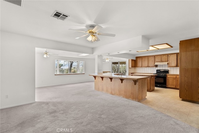 kitchen featuring a kitchen bar, black stove, tasteful backsplash, a center island, and ceiling fan