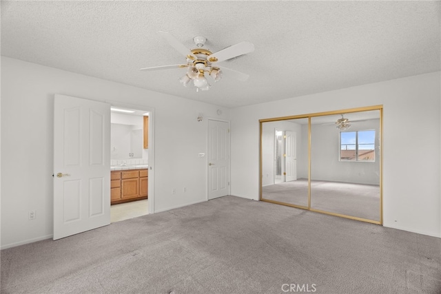 unfurnished bedroom with a closet, ensuite bathroom, light carpet, and a textured ceiling