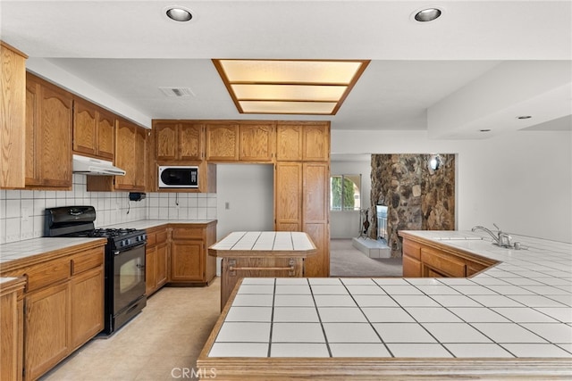 kitchen with sink, black range with gas cooktop, tile counters, built in microwave, and decorative backsplash