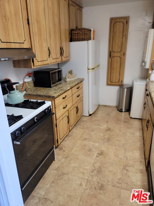 kitchen featuring extractor fan, washer / clothes dryer, light stone countertops, and white appliances