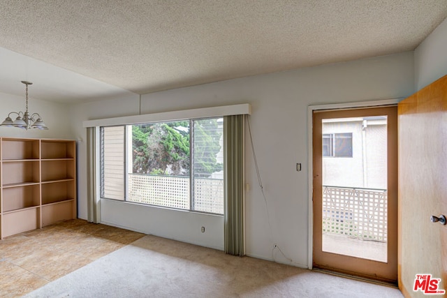 spare room with a notable chandelier, a textured ceiling, and light colored carpet