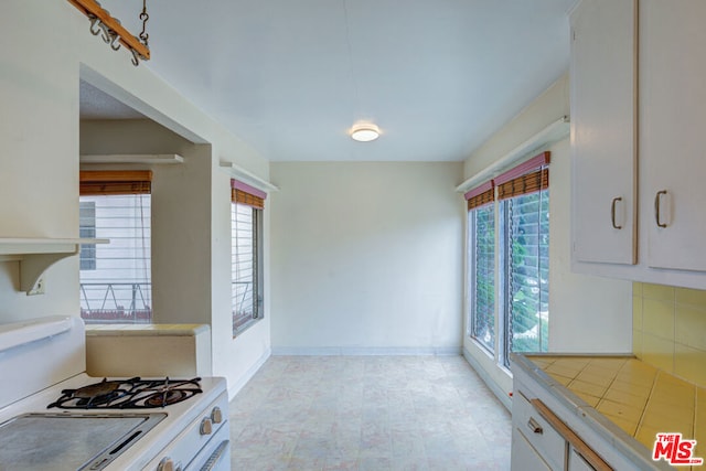 kitchen featuring white range with gas stovetop, a healthy amount of sunlight, backsplash, and white cabinets