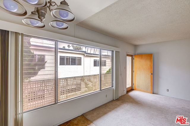 carpeted empty room featuring a textured ceiling and an inviting chandelier