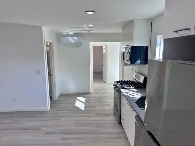 kitchen with a wall unit AC, white cabinetry, stainless steel appliances, and light wood-type flooring