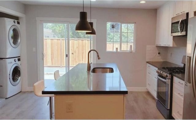 kitchen with white cabinetry, stacked washer and clothes dryer, stainless steel appliances, hanging light fixtures, and sink