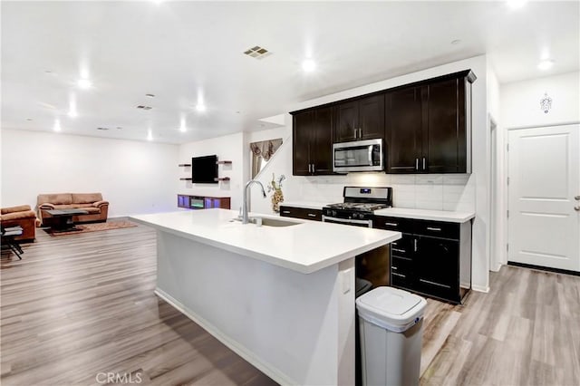 kitchen featuring a center island with sink, light hardwood / wood-style floors, decorative backsplash, appliances with stainless steel finishes, and sink