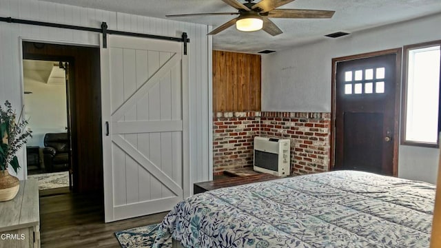 bedroom with wood walls, a barn door, a textured ceiling, dark hardwood / wood-style flooring, and ceiling fan