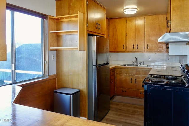 kitchen featuring sink, backsplash, black electric range oven, stainless steel refrigerator, and light hardwood / wood-style flooring