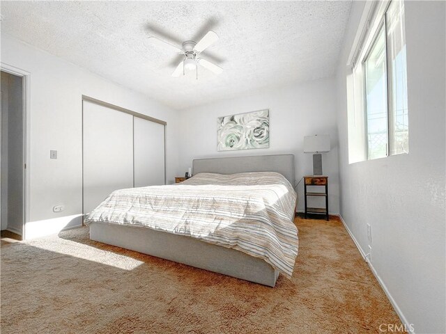 carpeted bedroom with a textured ceiling, ceiling fan, and a closet