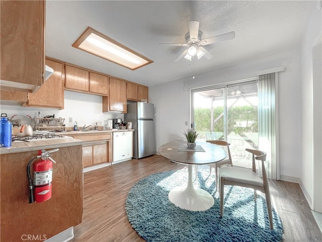 kitchen with light countertops, light brown cabinets, white dishwasher, and freestanding refrigerator