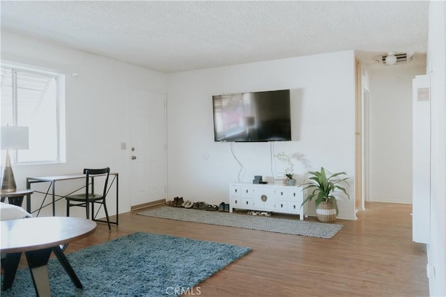 living area with visible vents, a textured ceiling, and wood finished floors