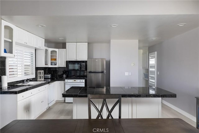 kitchen with light hardwood / wood-style flooring, backsplash, white appliances, a breakfast bar area, and white cabinets