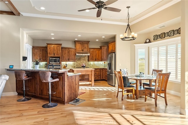 kitchen with light hardwood / wood-style floors, tasteful backsplash, stainless steel appliances, and a kitchen bar