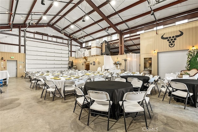 dining area featuring concrete floors, high vaulted ceiling, and wood walls