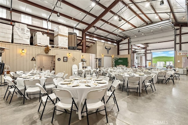 dining space with concrete floors, wooden walls, and high vaulted ceiling